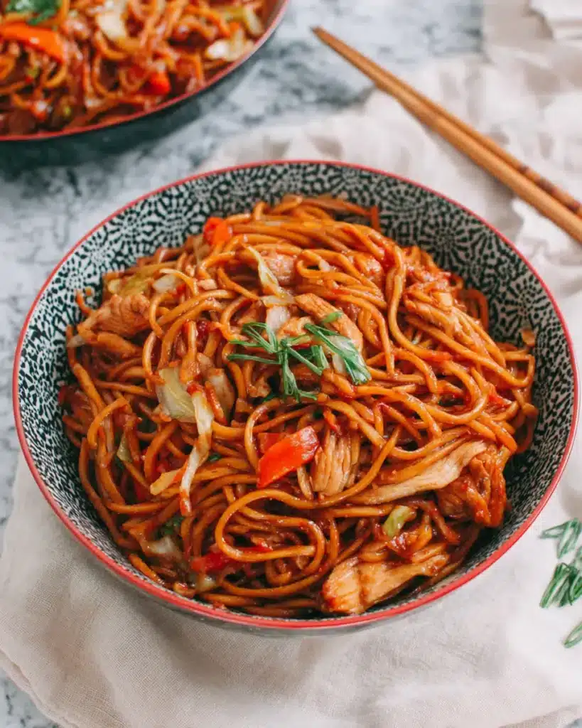 Overhead image of chicken lo mein served in a patterned ceramic bowl with chopsticks beside it.