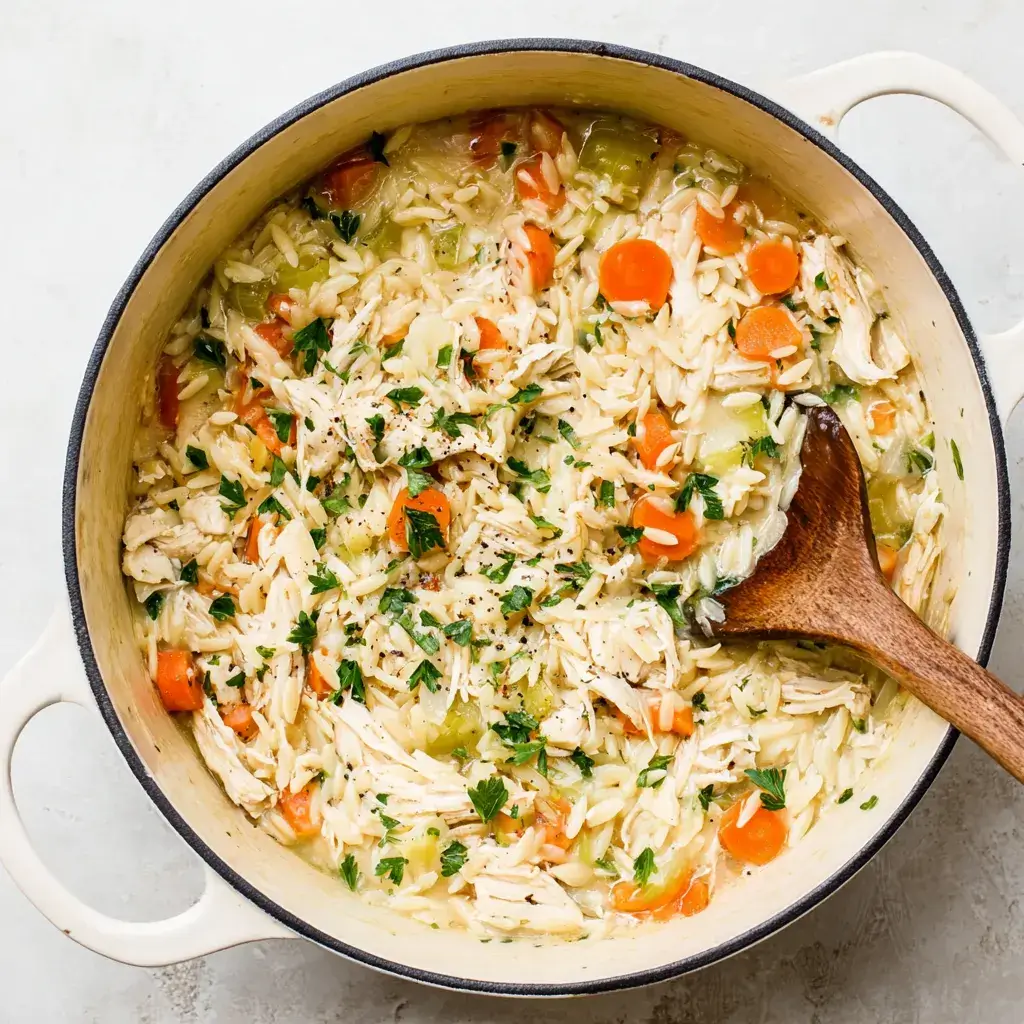 Creamy chicken orzo cooking in a white Dutch oven with carrots and celery