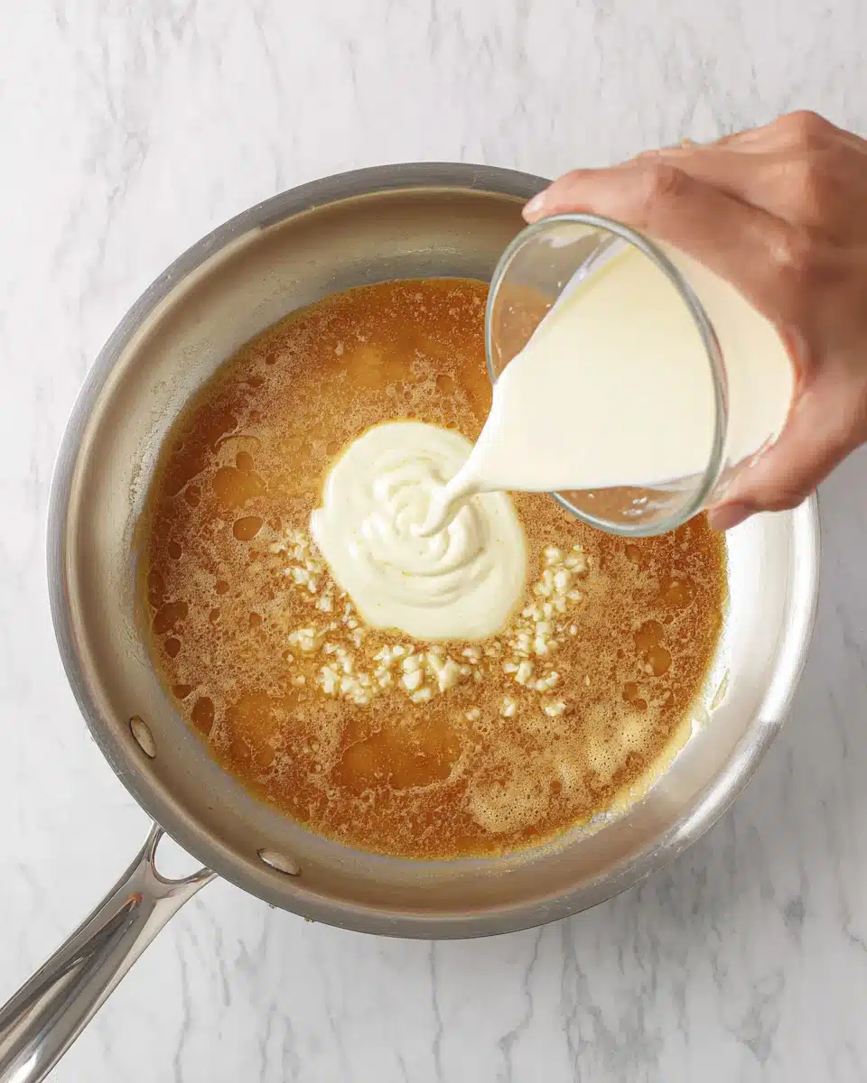Pouring heavy cream into a skillet with garlic and chicken broth to make creamy sauce.