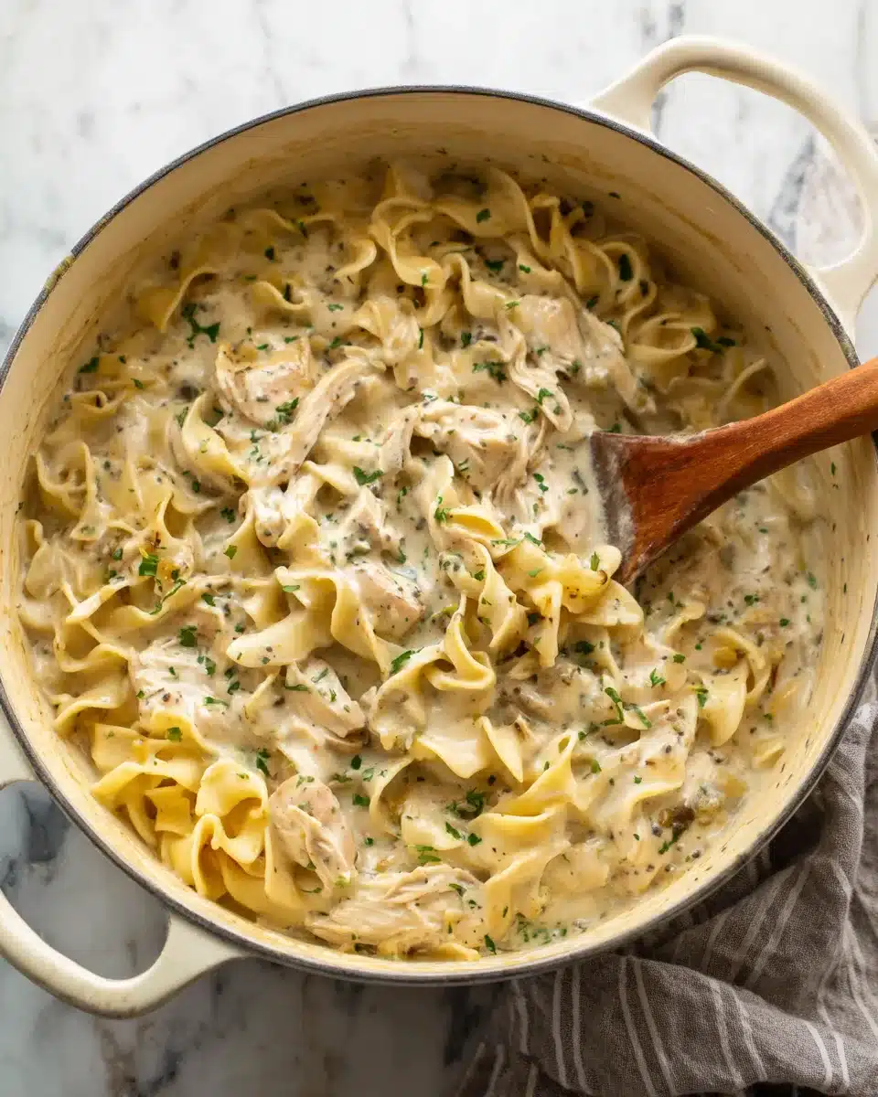 Creamy Chicken and Noodles in Pot A pot of savory chicken and noodles with a wooden spoon lifting creamy egg noodles and chicken.