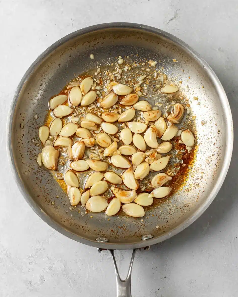 Garlic cloves sautéing in butter in a stainless steel pan with browned bits.