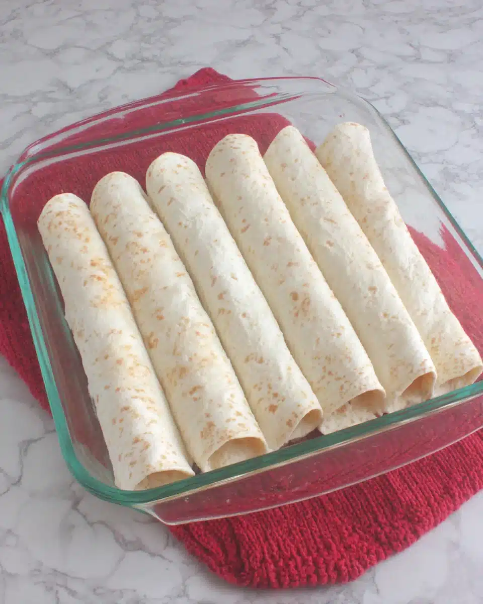 Rolled tortillas for creamy chicken enchiladas arranged in a glass baking dish